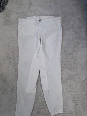 Vita ridbyxor med helskodd - Snygga vita ridbyxor med helskodd och bälteshällor. Klassisk design med fickor fram och en bakficka med dragkedja. Perfekta för träning eller tävling inom ridsport. Materialet är stretchigt och bekvämt för optimal rörelsefrihet. Har lite fläckar men som jag tror går bort snabbt med nått medel eller i nån grövre tvätt har aldrig använt dom osäker vart fläcken kommer ifrån 