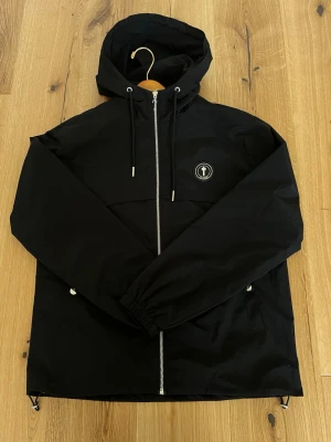 Trapstar Irongate T Windbreaker – Black (Nyskick) - Säljer en Trapstar Irongate T Windbreaker i svart.  Köpt ny för cirka 2800kr.   Jackan är i princip oanvänd och i nyskick.  Inga slitningar, fläckar eller tecken på användning.   • Modell: Irongate T Windbreaker • Färg: Svart • Skick: 9,5/10 (nyskick) • Storlek: M - passar storlek S också med lite mer relaxed fit.   Detta är ett drop från augusti 2022. Samma modell ligger på resell runt 2000 kr på StockX, vilket säger en del om efterfrågan.