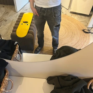 Replay anbass med slitningar - Säljer ett par grå jeans med flera fickor och slitningar på benen. Jeansen har en avslappnad passform och coola detaljer som dragkedjor och sömmar. Perfekta för en streetwear-look och passar till sneakers och t-shirt.