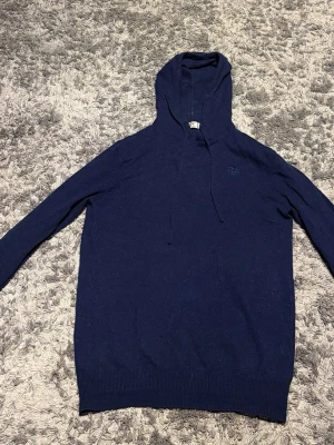 Bvaldi hoodie mörkblå - Mörkblå hoodie med huva och dragsko. Tillverkad i mjukt stickat material och har ribbade muddar vid ärmslut och nederkant. Enkel och stilren design med diskret broderad logga på bröstet. Perfekt för en avslappnad look. Finns ett litet hål i armhålan men inte super synligt!!! Ordinarie pris ligger den på 1199kr