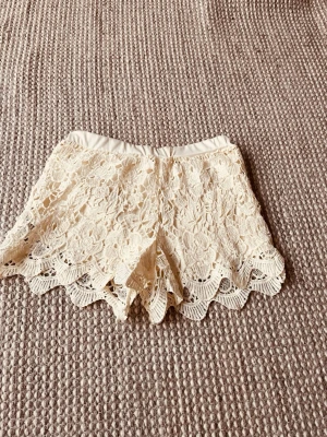 Beige spets-shorts med blommönster - Säljer ett par supervackra beige shorts med blommig spets och vågig kant. De har elastisk midja och är i fint skick. Perfekta för varma dagar när du vill ha en  trendig look. Står storlek XL i dem men passar som XS/S. Köpt från en annan säljer dem då dem är för stora för mig. (Personen jag köpte av sa att dem var i XXS) men de är ungefär Xs/S. Pris kan diskuteras!!
