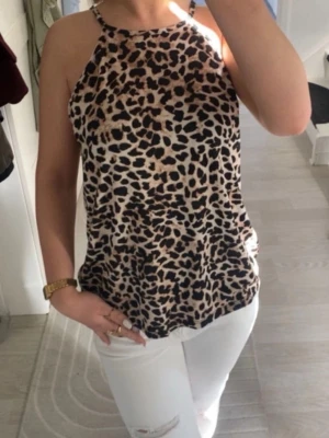 Leopardmönstrad linnetopp - Snygg ärmlös linnetopp med leopardmönster i beige och svart. Toppen har smala axelband och rak passform, perfekt för att lyfta vilken outfit som helst. Materialet känns lätt och luftigt.