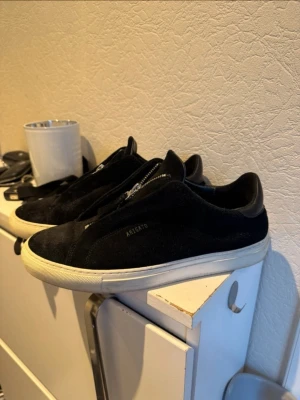 Svarta sneakers från Axel Arigato - Stilrena svarta sneakers från Axel Arigato i mocka med vit sula och dragkedja framtill istället för klassiska snören. Snygg minimalistisk design och diskret logga på sidan. Perfekta för dig som gillar en clean look. Har bara används några gånger , denna model säljs inte längre 