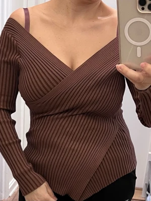 Brun omlottopp från SHEIN - Brun ribbad omlottopp från SHEIN med djup v-ringning och långa ärmar. Toppen har en asymmetrisk nederkant och sitter snyggt figurnära. Perfekt för dig som gillar trendiga detaljer och vill ha en unik topp i garderoben.