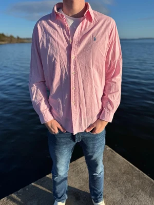 Rosa rutig skjorta från Ralph Lauren - Klassisk rosa skjorta från Ralph Lauren med diskret rutigt mönster och broderad logga på bröstet. Skjortan har lång ärm, knappar framtill och normal passform. Storlek L men passar M.Perfekt till jeans eller chinos för en clean och stilren look. Pris 379kr men går att sänka vid snabb och smidig affär💙 //Studio II Resell