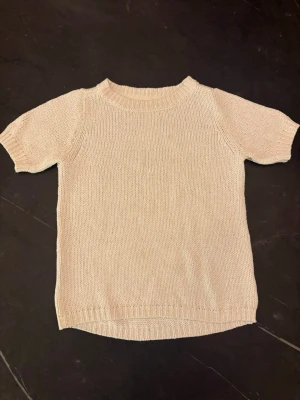 Beige stickad t-shirt från STOCKH LM - Snygg krämvit stickad t-shirt från STOCKH LM i storlek XS. Tröjan har korta ärmar, rund halsringning och ribbade kanter. Perfekt för dig som gillar en enkel och stilren look men endå något speciellt i med att den glittrar lite❤️
