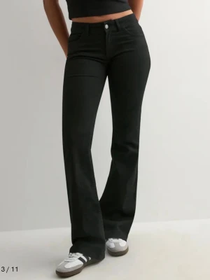 Svarta bootcut jeans från NA-KD - Snygga svarta bootcut jeans från Nelly  med låg/mellan midja. Jeansen har utsvängda ben och diskreta sömmar på bakfickorna. Perfekta att matcha med sneakers eller boots för en trendig look.