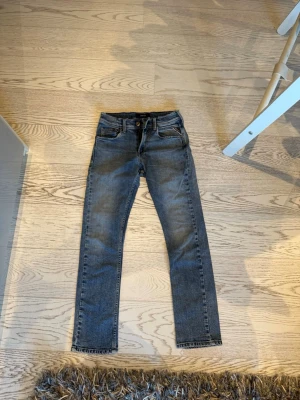 Blå slim fit jeans från Replay - Snygga blå slim fit jeans från Replay med klassisk femficksdesign och dragkedjegylf. Jeansen har en tvättad look med slitningar och är tillverkade i denim. Perfekta för en trendig och avslappnad stil.