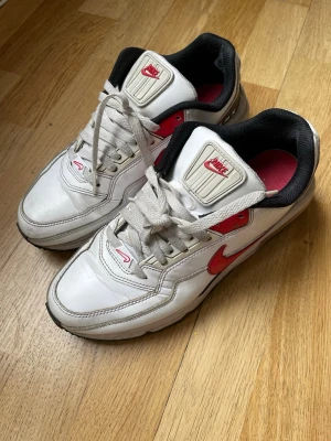 Nike Air Max LTD 3 - Nike Air Max LTD 3  i vitt läder med röda detaljer och svart insida.  Skorna har vita snören och AIRMAX-tryck på hälen. 