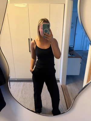 Svarta vida kostymbyxor i bomull - Säljer ett par svarta kostymbyxor med vid passform och hög midja. Byxorna är tillverkade i mjuk bomull och har en clean look med synliga detaljer. 