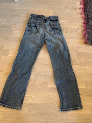 Blå bootcut jeans med kontrastsömmar - Säljer ett par blå bootcut jeans med tydliga kontrastsömmar och två bakfickor med dekorativa sömmar. Jeansen har en klassisk femficksdesign och är tillverkade i denim. Perfekta för en avslappnad och trendig look.