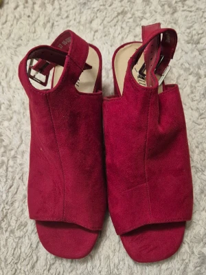 Vinröda sandaler från Alley - Snygga vinröda sandaler från Alley i mockaimitation. De har öppen tå, bred ovandel och justerbart spänne vid ankeln. Perfekta för dig som vill ha en trendig och bekväm look till sommaren.