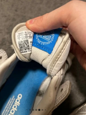 Vita Adidas Continental 80 sneakers - Säljer ett par klassiska vita Adidas Continental 80 sneakers med blå innersula och logga på plösen. Skorna har lågt skaft, snörning och är tillverkade i läder med perforerade detaljer på tån. Perfekta för en clean och retro look.