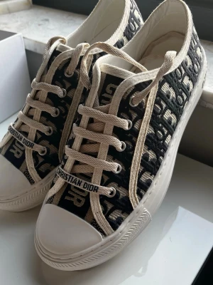 Dior Oblique låga sneakers - Snygga låga sneakers från Dior med klassiskt blått och vitt Oblique-mönster. Skorna har vita snören, vit sula och detaljer med 'CHRISTIAN DIOR' på sidan och hälen. Ovandelen är i textil och sulan i gummi. Perfekta för en trendig och exklusiv look.