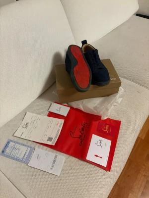 Mörkblå sneakers från Christian Louboutin - Snygga mörkblå sneakers från Christian Louboutin i mocka med klassisk röd sula. Skorna har svarta snören, diskret logga på sidan och en stilren design. Perfekta för dig som vill ha något exklusivt och trendigt i garderoben. Priset är inte huggit i sten