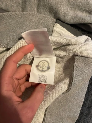 Grå Moncler sweatshirt med tryck - Snygg grå sweatshirt från Moncler med 3D-tryckt logga i rött och svart på bröstet. Tröjan har quiltade detaljer längs ärmarna och ribbade muddar. Perfekt för dig som gillar streetwear och exklusiva märken.