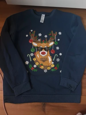 Blå jultröja med ren och tryck - Mörkblå sweatshirt med ett  tryck av en ren med solglasögon. Perfekt för julmys och att sticka ut på julfesten. Rund hals och ribbade muddar. Mysigt material strl 160-170.