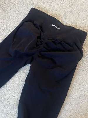 Svarta seamless tights från DFYNE - Säljer ett par sprillnans nya svarta seamless tights från DFYNE med stretchigt material. Använda 1 gång!! Perfekta för gymmet eller träning, med diskret logga framtill i vitt. Materialet är mjukt och följsamt för maximal komfort.