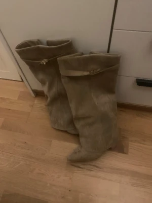 Beige höga boots - Säljer ett par snygga beige stövlar i mocka med högt skaft och dekorativt band upptill. Dessa boots är aldrig använda och jag betalade 1000kr för de. Priset går att diskuteras❤️