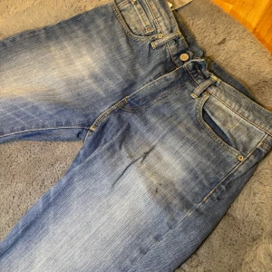 Levi's 501 ljusblå jeans straight fit - Säljer ett par klassiska Levi's 501 jeans i ljusblå tvätt med snygga slitningar och raka ben. Storleken är 31/32. Jeansen har fem fickor, knappgylf och den ikoniska läderpatchen bak. Perfekt för dig som gillar tidlös streetstil och vill ha ett par jeans med autentisk vibe. De har en lite fläckar som försökts räddas med slitningar men kan inte säga att det blev mycket bättre😅