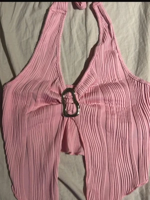 Halterneck topp  - Ljusrosa ribbad halterneck-topp med öppen front och dekorativ metallring i mitten ger en snygg och edgy vibe. Croppad modell som framhäver midjan och passar perfekt till höga jeans eller kjol. En riktig statement-topp för fest eller sommarkvällar.(ifrån shein)  