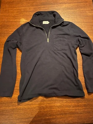 Mörkblå halvzip tröja från East West - Snygg mörkblå långärmad tröja från East West med halvzip och hög krage. Tröjan har en bröstficka och är gjord i mjukt, tunnt material som passar perfekt till lager på lager. Enkel och stilren design som funkar till det mesta, och perfekt nu till våren! ☀️🌳