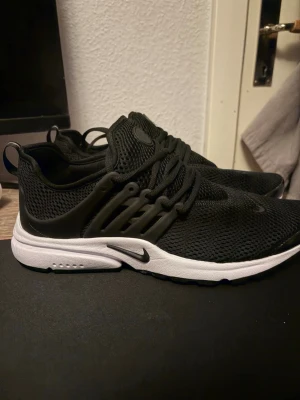 Nike Air Presto svarta sneakers - Säljer ett par svarta Nike Presto sneakers med vit sula. Skorna har en mesh-överdel för bra ventilation, elastiska snören och plastdetaljer på sidorna för extra stöd. Perfekta för dig som gillar stilrena och bekväma sneakers med sportig känsla. Köpte dom fast dom passade inte. 