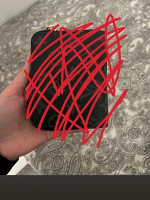 Svart plånbok med dragkedja - Snygg svart plånbok i rektangulär form med dragkedja runtom. Plånboken har en stilren look och verkar vara tillverkad i ett tåligt material, troligen konstläder. Perfekt storlek för att få plats med kort och sedlar.dragkedjan är lite trög 