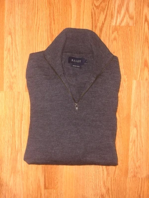 Mörkgrå merinoulltröja från Riley - Snygg mörkgrå stickad tröja från Riley i mjuk merinoull. Tröjan har halv dragkedja och hög krage, perfekt för lager på lager. Enkel och stilren design som passar till det mesta.