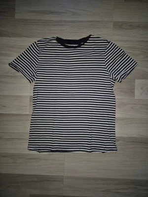 Randig svartvit t-shirt - Snygg svartvit randig t-shirt med korta ärmar och rund hals. Perfekt basplagg som passar till det mesta. Tillverkad i mjuk bomull för skön känsla hela dagen. Den har 2 små hål i ryggen, se bild.