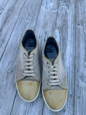 Beige DBB1 sneakers från Lanvin - Snygga sneakers från Lanvin i beige mocka med beige gummitå och vita sulor. Skorna har klassisk låg profil, vita snören och diskret logga på sulans undersida. Okej skick, välanvända, se skador på bilderna. Endast skor medföljer, ingen låda eller dustbags. UK9/EU43. Tveka inte att höra av dig vid frågor (: