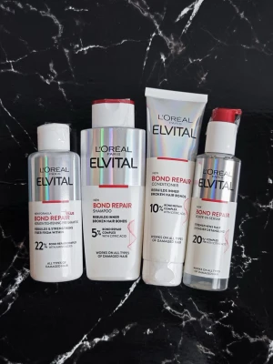 L'Oréal Elvital Bond Repair set - Fyra produkter från L'Oréal Elvital Bond Repair-serien: schampo, balsam, leave-in serum och förbehandling. Flaskorna är vita med holografiska och röda detaljer. Innehåller citronsyra och är anpassade för skadat hår. Passar alla hårtyper och har moderna, stilrena förpackningar.