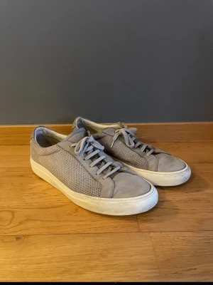 Common Projects sneakers gråa Storlek 43 - Ett par Common Projects sneakers i stilren design. Storlek 43  Använda men fortfarande i bra skick. Viss användning finns (se bilder), men inget som påverkar funktionen. Klassisk modell som passar till det mesta.  Nypris ca 4000- 5000 tusen  Säljes till bra pris vid snabb affär. Hör av dig vid frågor eller fler bilder.