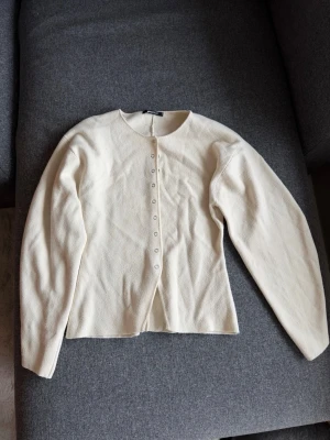 Vit tröja med knappar - Stilren vit tröja med rund urringning. Tröjan har en figutsydd passform och knäpps framtill med små knappar