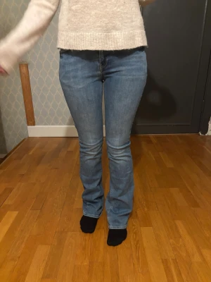 Blå bootcut jeans med hög midja - Snygga blå bootcut jeans med hög midja och klassiska fem fickor. Jeansen har en lätt utsvängd passform nertill och är tillverkade i ett stretchigt denimtyg som sitter bekvämt. Perfekta för en trendig och avslappnad look.