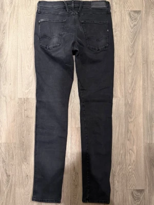 Replay Anbass Hyperflex Svarta Jeans W33/L34 Slim Fit - Replay Anbass Hyperflex svarta jeans i stretchigt och bekvämt material, clean och stilren modell som sitter slim och funkar till det mesta, storlek W33/L34, midja 41 cm, ytterbenslängd 111,5 cm, benöppning 15,5 cm, modellen är 185 cm och väger 65 kg, i fint skick.