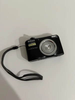 Nikon COOLPIX digitalkamera svart - Snygg svart Nikon COOLPIX A10 digitalkamera med 16 megapixlar och 5x optisk zoom. Kompakt design i plast och metall, med stor display och enkla knappar på baksidan. Perfekt för att fånga minnen med stil. Kameran är i superskick då den knappt är använd alls sedan 2016 då den köptes.