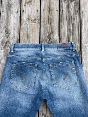 Blå raka jeans från Dondup - Säljer ett par klassiska blå jeans från DG med raka ben och snyggt slitna detaljer. Jeansen har två bakfickor med dekorativa sömmar och bälteshällor. Perfekta för en avslappnad och trendig look.