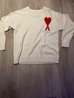 Ami Sweater  - 🔥 AMI Paris sweater – stilren och trendig! ❤️    Säljer en vit AMI sweater med den klassiska röda Ami de Cœur-loggan (hjärta med A) på bröstet. En väldigt populär och stilren designertröja som passar till nästan allt – jeans, cargos eller kostymbyxor.    👕 Detaljer:   • Märke: AMI Paris   • Modell: Sweater   • Färg: Vit med röd logga ❤️   • Mjuk och bekväm stickad kvalitet   • Stilren och minimalistisk design   • Väldigt fint skick   • Storlek: S men passar M/L bättre   