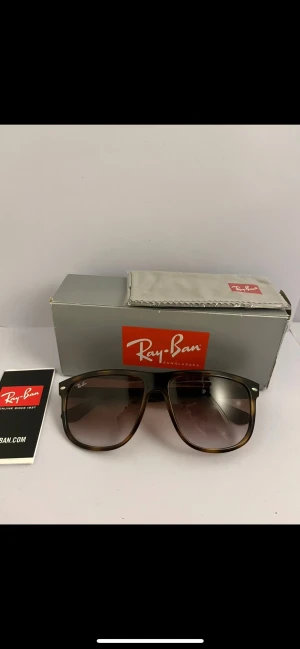 Rayban boyfriend - Snygga solglasögon från Ray-Ban med brunmelerad båge och fyrkantig form. Glasen är tonade i brunt och bågarna har en klassisk retrovibe. Perfekta för att lyfta din stil med en ikonisk accessoar från ett av de mest kända märkena.