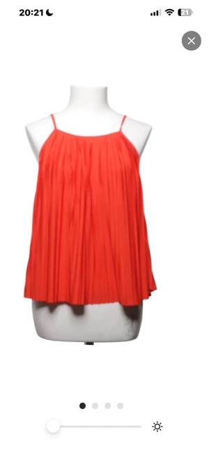 Röd plisserad topp med smala axelband - Snygg röd plisserad topp med tunna axelband och lös passform. Perfekt för dig som gillar en luftig och trendig stil. Materialet ser ut att vara lätt och bekvämt, vilket gör den enkel att bära under varma dagar.