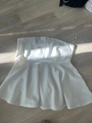 Vit axelbandslös bandeautopp - Säljer en snygg vit bandeautopp med axelbandslös design och lätt utsvängd nederdel. Toppen har en stilren look och är perfekt för sommarens alla tillfällen. Materialet känns mjukt och följsamt mot huden.