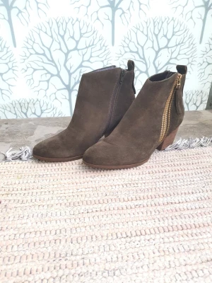 Gröna stövletter med guldzip - Snygga gröna stövletter i mocka med dekorativ guldglittrande dragkedja på sidan och stabil träklack. Skorna har rundad tå och diskret pull-tab baktill. Perfekt för dig som gillar stilrena boots med en twist.