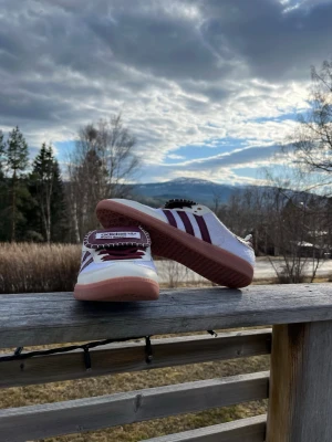 Adidas Samba x Wales Bonner - Snygga Adidas sneakers i vitt med klassiska vinröda ränder på sidorna och matchande detaljer. Skorna har en låg profil och gummisula i ljusbrunt. Ovandelen är i textil och mocka, med Adidas x Wales Bonner logga på plösen. Perfekta för en stilren och sportig look. Skriv för mer info ℹ️ 
