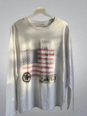 Graphic long sleeve tee shirt - Vit långärmad t-shirt med tryck av amerikanska flaggan och text i svart och rött, samt 18+ symbol och arabiska tecken. Rund hals och relaxed fit, perfekt för dig som gillar statement-plagg.