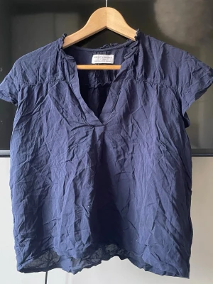 Mörkblå blus från Holly & Whyte - En mörkblå blus från Holly & Whyte med korta ärmar och v-ringad hals. Blusen har en avslappnad passform och lätt rynkad krage. Tillverkad i ett tunt, mjukt tyg som känns luftigt och bekvämt. Lite skrynklig men går lätt att fixa. Har några fläckar som borde gå bort i tvätten❣️