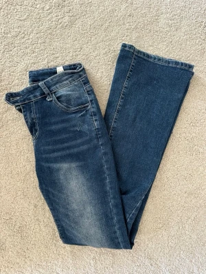Mörkblå bootcut jeans - Snygga mörkblå bootcut jeans med lätt slitning framtill och på bakfickorna. Lågmidjade. Klassisk femficksmodell med normal midja och dragkedja. Jeansen är tillverkade i stretchigt denim för extra komfort och har en tidlös look.