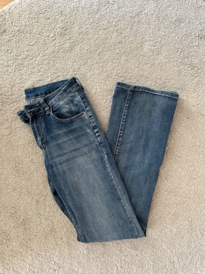 Blå raka jeans med vintagekänsla - Säljer ett par klassiska blå jeans med låg midja. Jeansen har fem fickor, normal midja och subtila tvättade partier framtill och baktill. Perfekta för en avslappnad och stilren look.