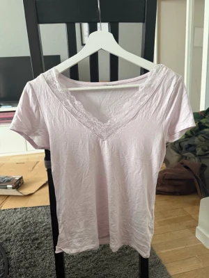 Två v-ringade toppar med spets - Säljer två snygga toppar i ljusrosa och mörkbrun färg. Båda har v-ringning med spetsdetaljer och korta ärmar. Perfekta att styla till jeans eller kjol för en trendig look.