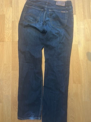 Mörkblå jeans från Mustang - Snygga mörkblå jeans från Mustang med raka ben och klassiska bakfickor med kontrastsömmar. Jeansen har läderpatch med logga bak i midjan och är tillverkade i denim. Perfekta för en avslappnad och stilren look.